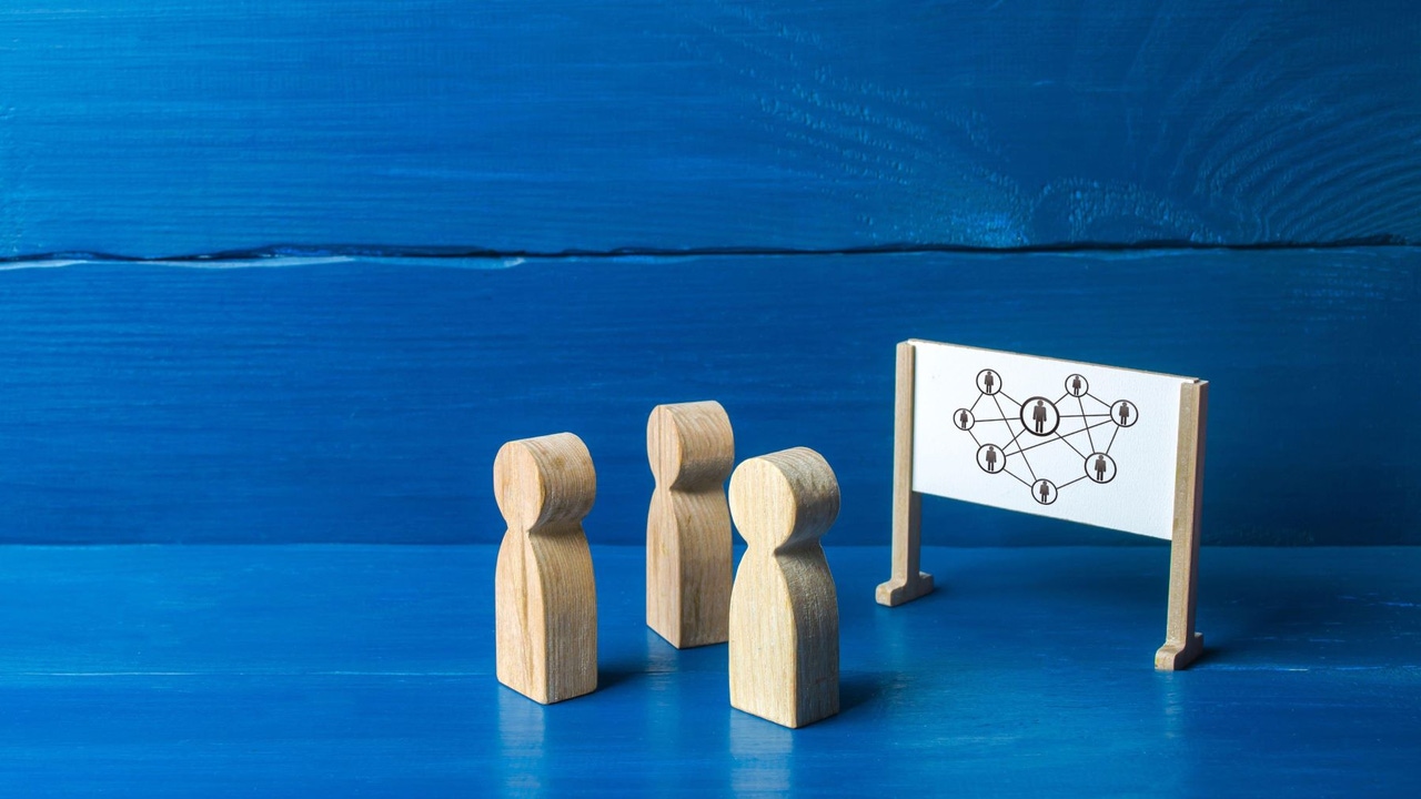 Three wooden figures representing people in front of a whiteboard
