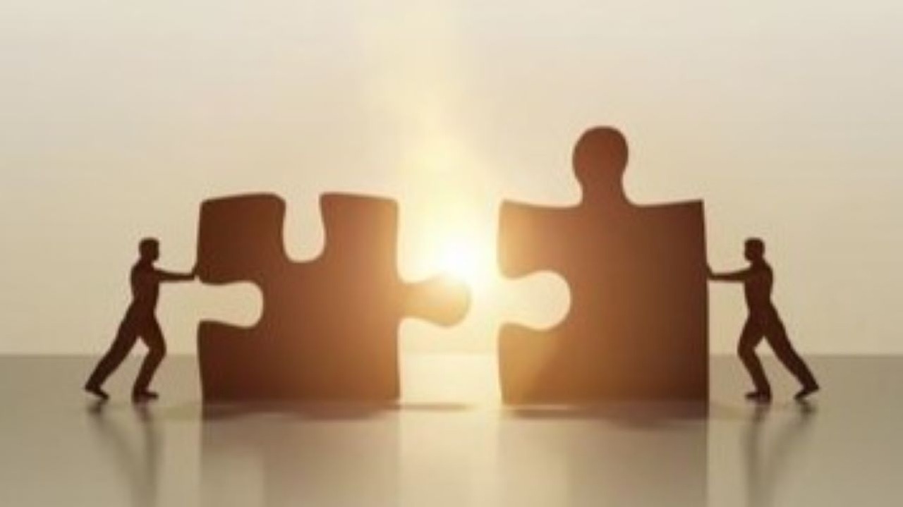 Silhouettes of two people pushing two giant puzzle pieces together Silhouettes of two people pushing two giant puzzle pieces together