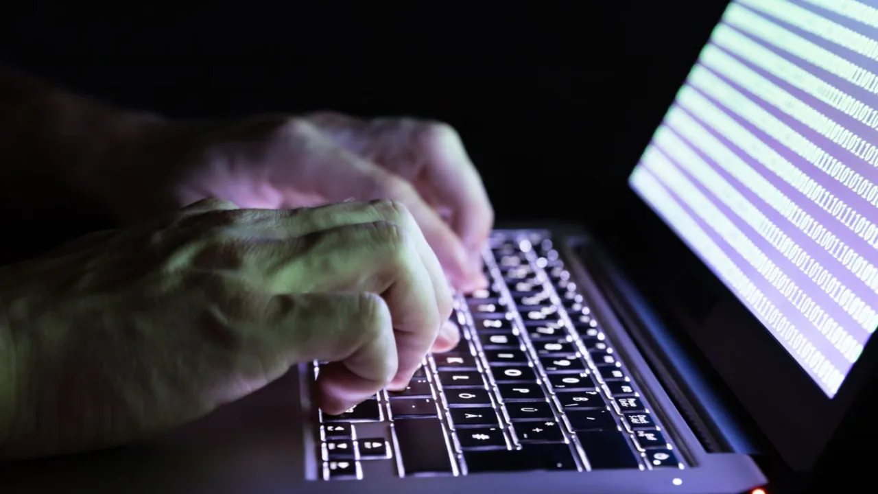 Hands typing at a computer keyboard with a series of ones and zeroes on the screen.