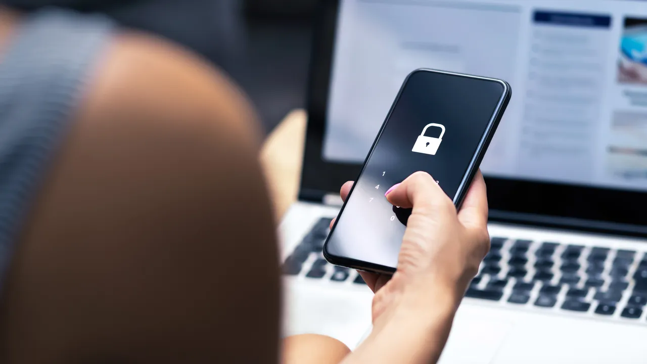A person typing a PIN code into their phone, at their desk.