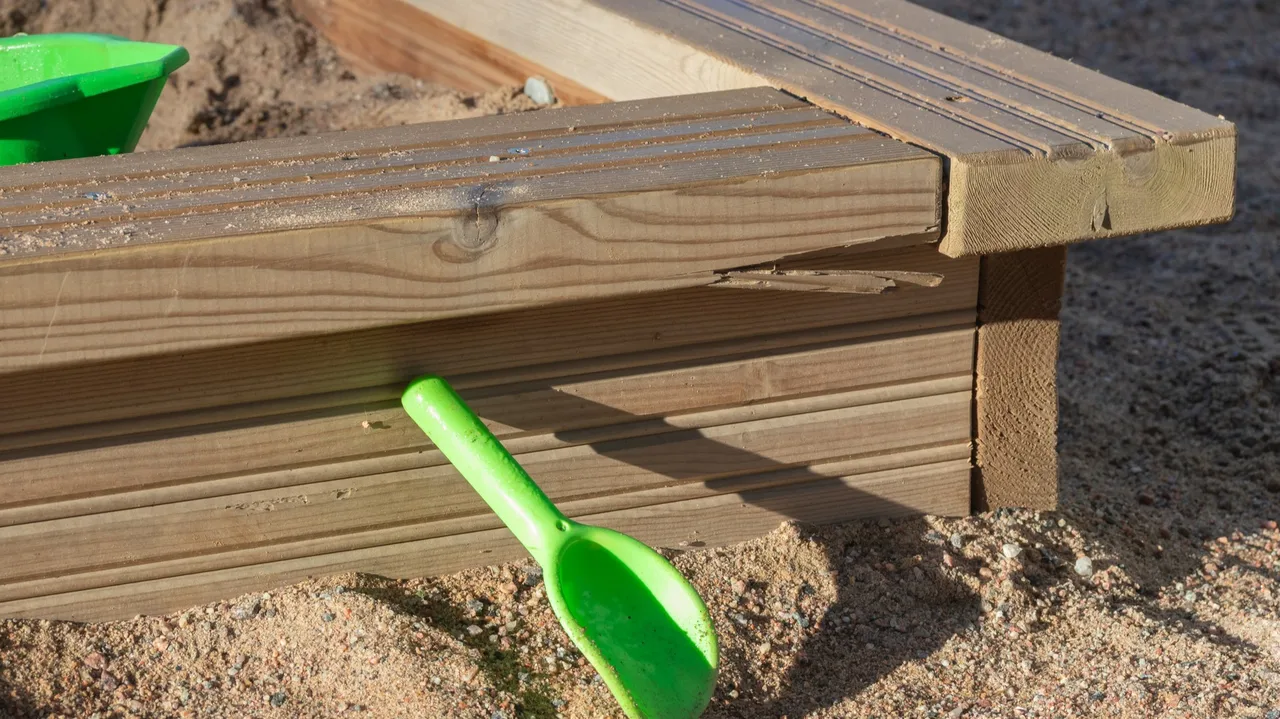 Green toy shovel leaning against a wood-framed sandbox Green toy shovel leaning against a wood-framed sandbox