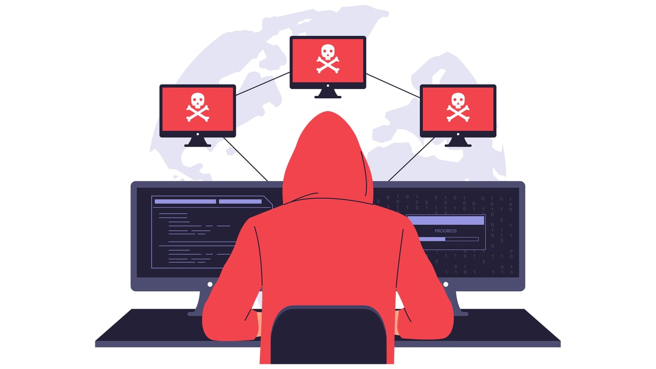 An illustration of a botnet cyberattack; attacker in a red hoodie sits at a computer with several screens around him showing skull and crossbones An illustration of a botnet cyberattack; attacker in a red hoodie sits at a computer with several screens around him showing skull and crossbones
